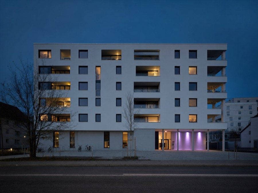 Beispielmotiv: Wohnneubau mit weißem Putz und dunklen Fensterrahmen in der Dämmerung