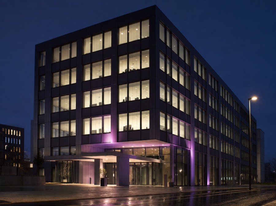Beispielmotiv: Bürogebäude mit Glasfassade und violett angestrahltem Eingang am Abend